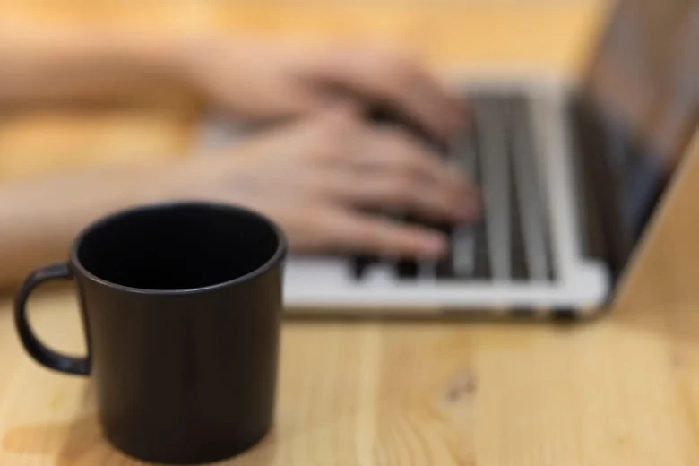 Pessoa digitando em um laptop sobre uma mesa com café, representando o trabalho de redator freelancer online
