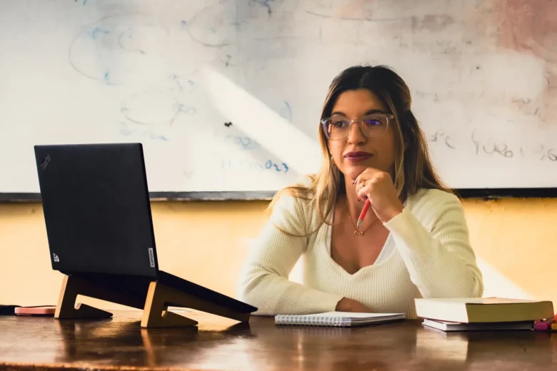 Empreendedora trabalha em laptop sobre mesa doméstica ao lado de caderno com anotações financeiras