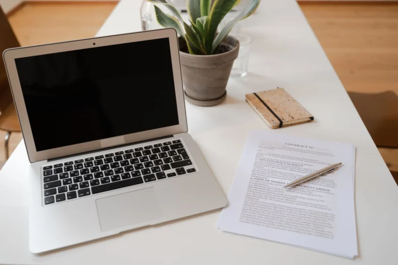 Revisor lê e corrige um texto em um laptop, com caneta e caderno aberto sobre a mesa