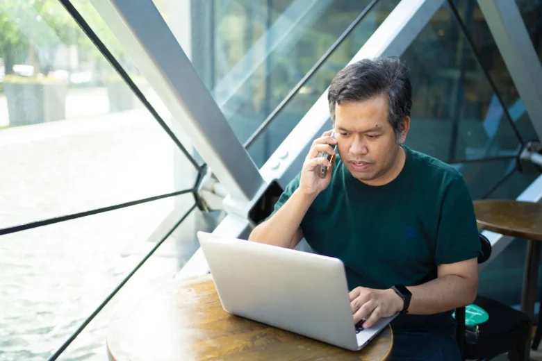 Profissional autônomo organiza agenda de serviços no notebook enquanto conversa com cliente pelo celular
