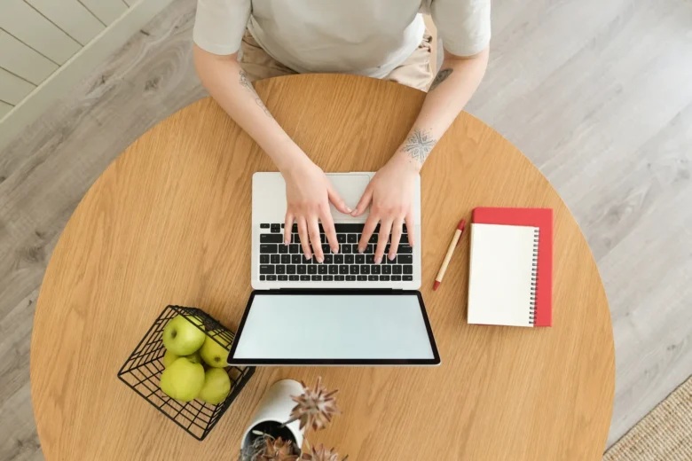 Homem trabalhando como freelancer em um laptop, em uma mesa doméstica com caderno de anotações ao lado