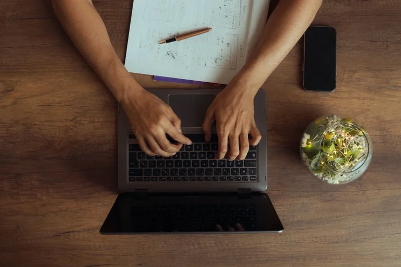 Mulher trabalhando em home office com notebook e caderno de anotações sobre uma mesa clara