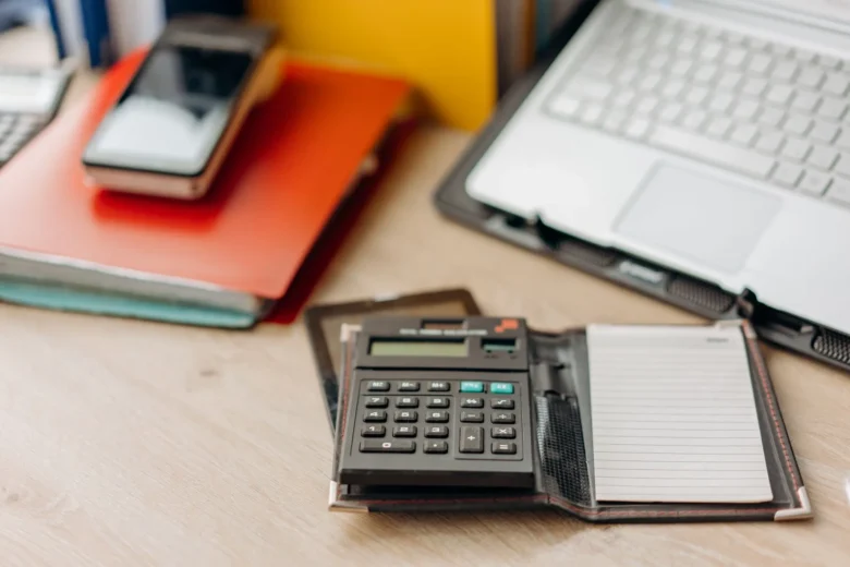 Caderno com cálculos de preço por hora ao lado de uma calculadora sobre uma mesa de trabalho
